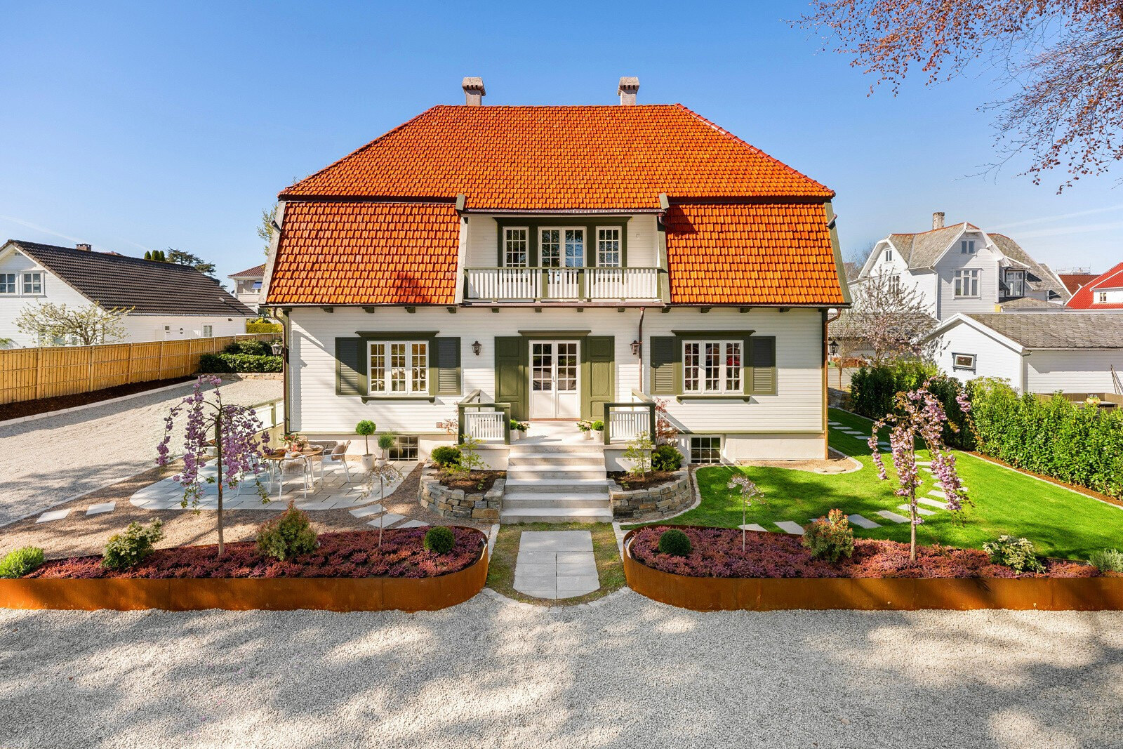 Klassisk hvit villa med rødt tegltak, grusgårdsplass og plantebed innrammet i cortenstål